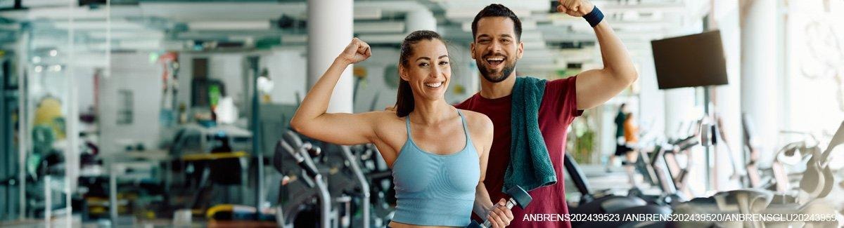 Casal adulto na academia, sorrindo, mostrando seus músculos