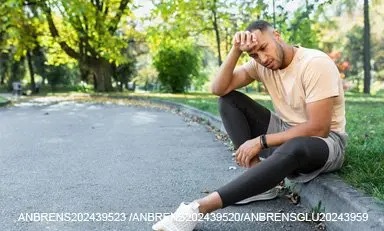 corpo de uma pessoa em roupas esportivas, sentado na calçada de uma grama ao ar livre