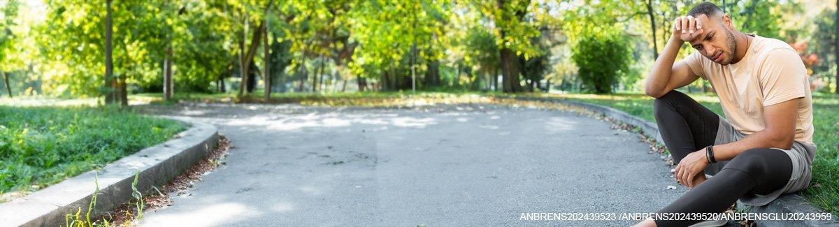 corpo de uma pessoa em roupas esportivas, sentado na calçada de uma grama ao ar livre