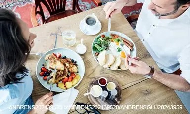 Casal de adultos comendo um café da manhã saudável de: ovos, salsicha, pão, morangos, mirtilos, torradas francesas e mais.