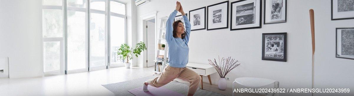 Mulher jovem em um apartamento iluminado, exercitando-se, respirando profundamente, transmitindo saúde, equilíbrio e serenidade.
