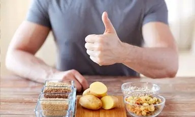 Pessoa em uma mesa, em frente a diferentes alimentos que fornecem carboidratos.