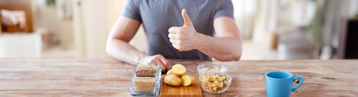 Pessoa em uma mesa, em frente a diferentes alimentos que fornecem carboidratos.