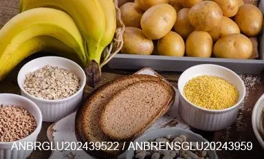 Pessoa em uma mesa, em frente a diferentes alimentos que fornecem carboidratos.