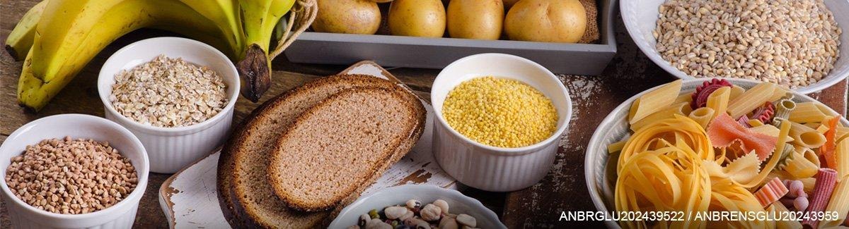 Pessoa em uma mesa, em frente a diferentes alimentos que fornecem carboidratos.