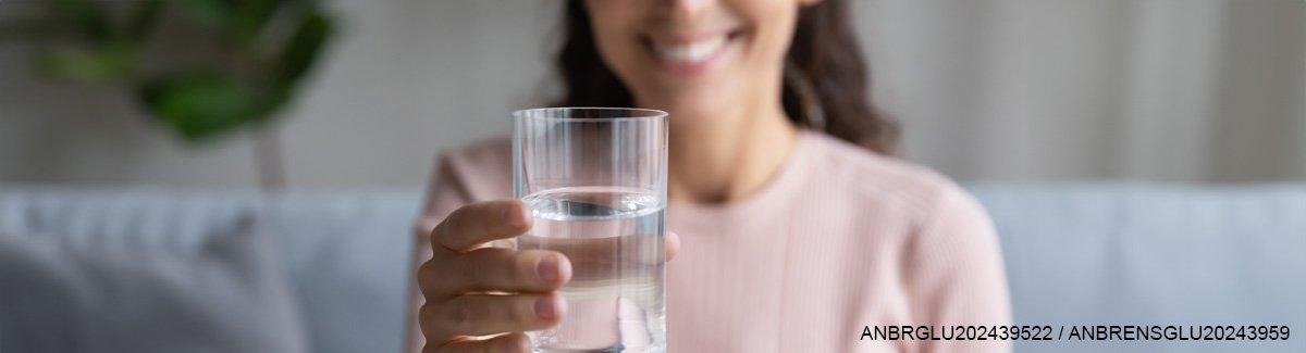 Pessoa segurando um copo de água, sorrindo, evocando os benefícios da hidratação para a saúde.