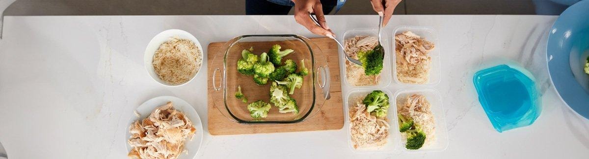 Mulher empacotando quatro almoços para levar com brócolis, arroz e frango.
