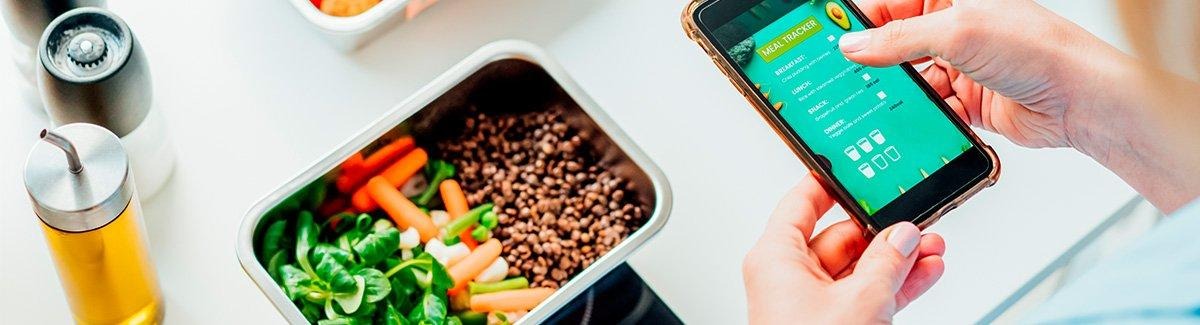 Mulher utilizando um aplicativo de registro de refeições com um almoço à sua frente em uma mesa.