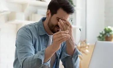 Homem segurando as têmporas com expressão de dor, segurando os óculos com a outra mão