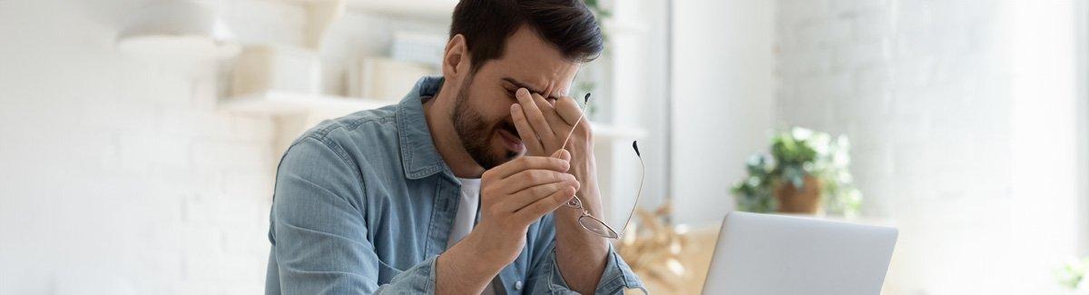 Homem segurando as têmporas com expressão de dor, segurando os óculos com a outra mão