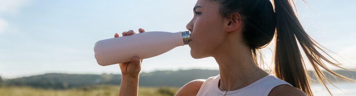 Mulher se hidratando ao pôr do sol