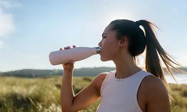 Mulher se hidratando ao pôr do sol