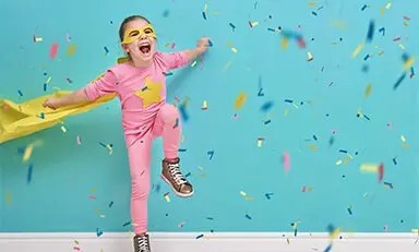 Menina com rabos de cavalo e suéter amarelo lendo um livro ao lado de um adulto