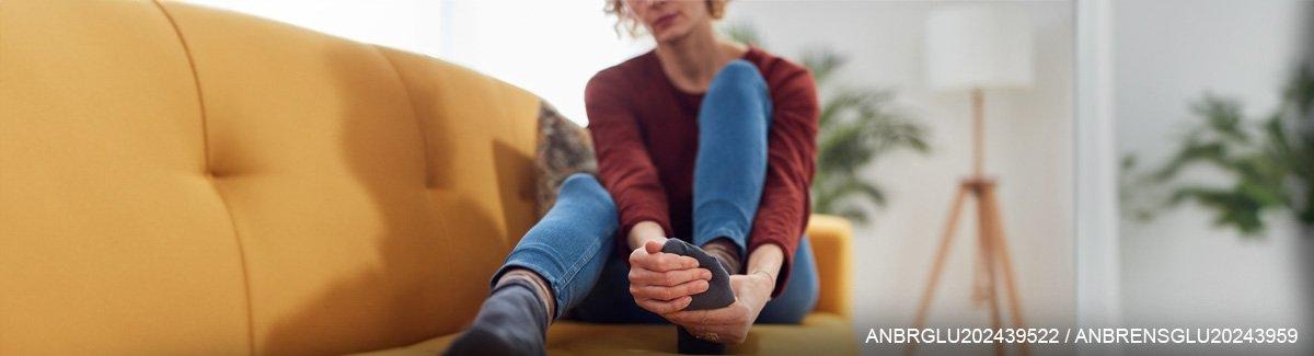 Mulher sentada em um sofá segurando seu pé.